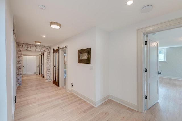 hall with a barn door, baseboards, and light wood-style floors