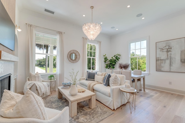 living area featuring a notable chandelier, visible vents, light wood-type flooring, and ornamental molding