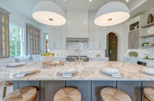 kitchen with light stone counters, wall chimney exhaust hood, crown molding, and open shelves