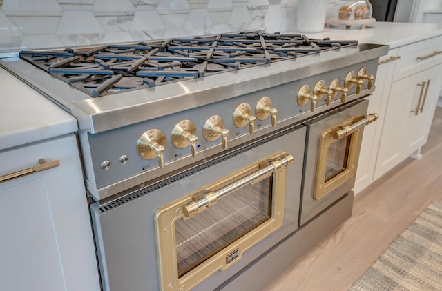 details featuring white cabinetry, range with two ovens, light wood finished floors, and backsplash