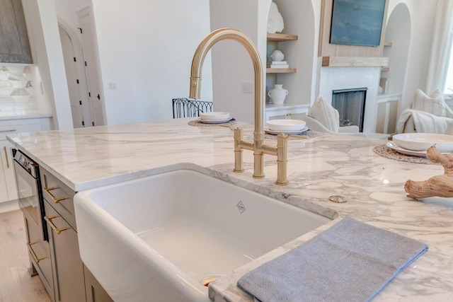 kitchen with dishwashing machine, built in shelves, light stone countertops, a fireplace, and a sink