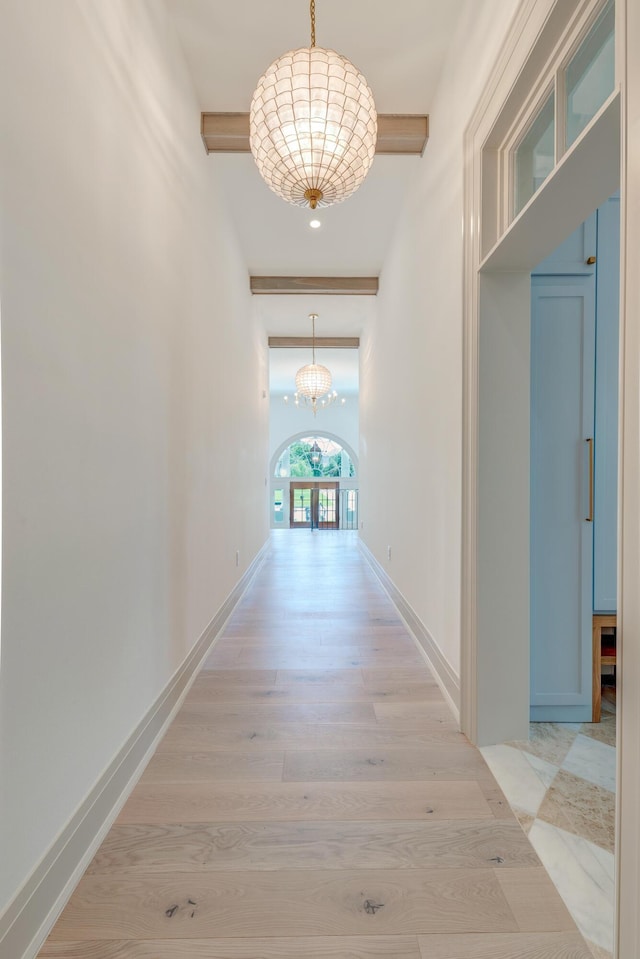 hall featuring an inviting chandelier, light wood-style flooring, beamed ceiling, and baseboards