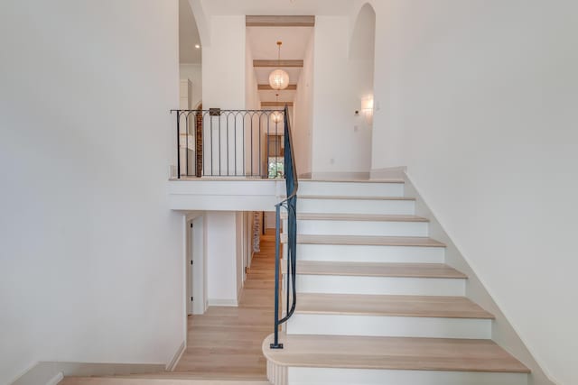 staircase featuring baseboards, arched walkways, wood finished floors, and a towering ceiling