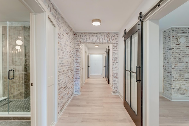 hallway with a barn door, brick wall, baseboards, and light wood-style floors