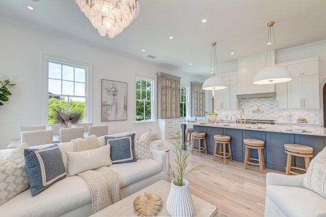 living area featuring light wood finished floors, visible vents, crown molding, recessed lighting, and a notable chandelier