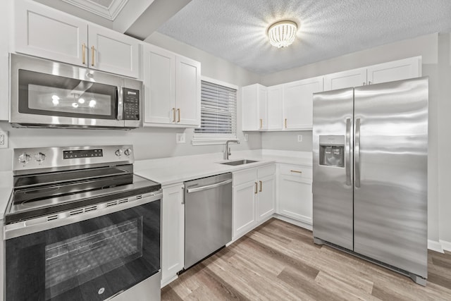 kitchen with a textured ceiling, light hardwood / wood-style floors, white cabinetry, appliances with stainless steel finishes, and sink