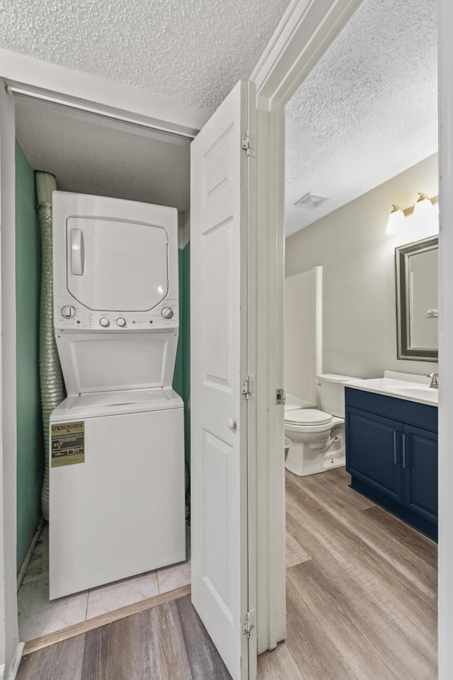 washroom with sink, light hardwood / wood-style floors, stacked washer / dryer, and a textured ceiling