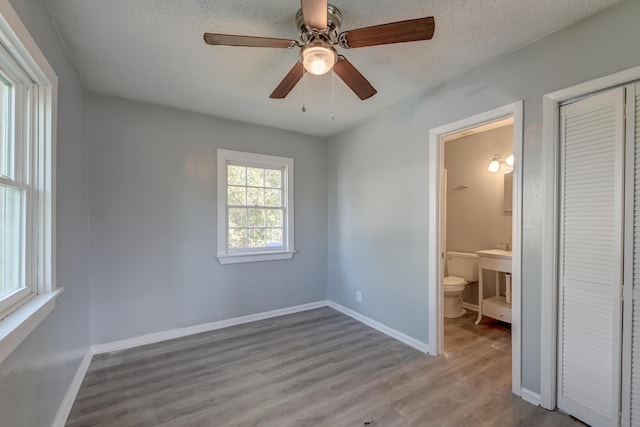unfurnished bedroom featuring a textured ceiling, baseboards, a closet, and wood finished floors