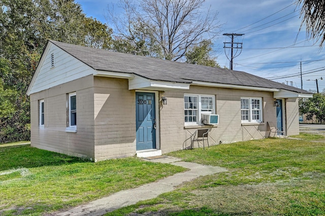 bungalow with cooling unit, a shingled roof, brick siding, and a front lawn