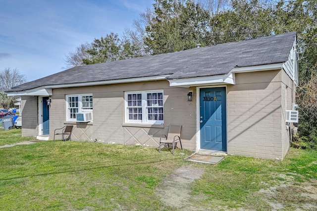 view of front of property featuring a front lawn, cooling unit, a shingled roof, and concrete block siding