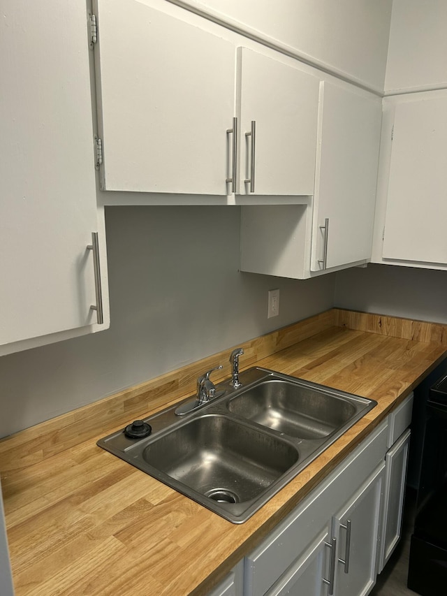 kitchen with a sink, butcher block counters, and white cabinets