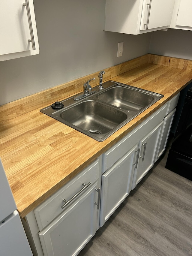 kitchen with a sink, butcher block counters, dark wood-type flooring, and white cabinets