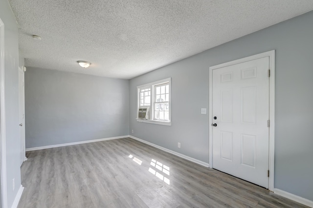 spare room with cooling unit, a textured ceiling, wood finished floors, and baseboards