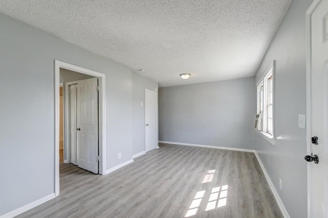 spare room with a textured ceiling, wood finished floors, and baseboards