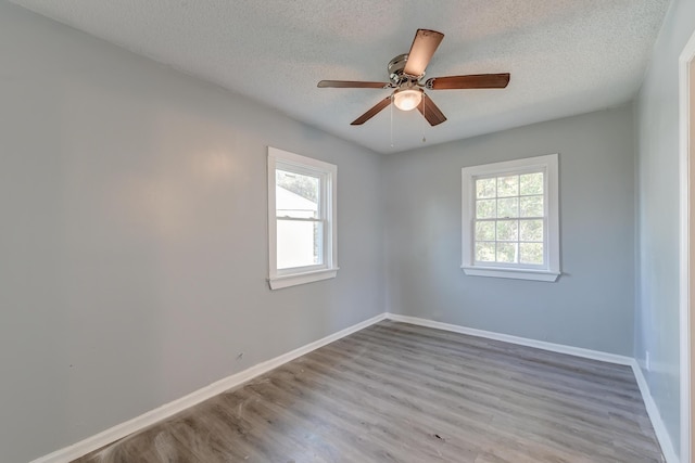 spare room with a wealth of natural light, wood finished floors, baseboards, and a textured ceiling