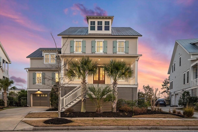 raised beach house featuring metal roof, an attached garage, covered porch, concrete driveway, and stairway