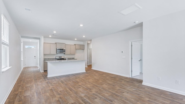 kitchen featuring white range with electric cooktop, a kitchen island with sink, hardwood / wood-style floors, and light stone counters