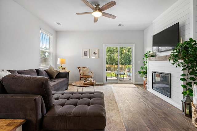 living room with wood finished floors, a glass covered fireplace, visible vents, and a healthy amount of sunlight