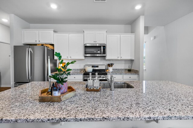 kitchen with white cabinets, decorative backsplash, appliances with stainless steel finishes, and light stone countertops