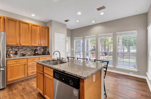 kitchen featuring dark hardwood / wood-style flooring, light stone counters, stainless steel appliances, sink, and a center island with sink