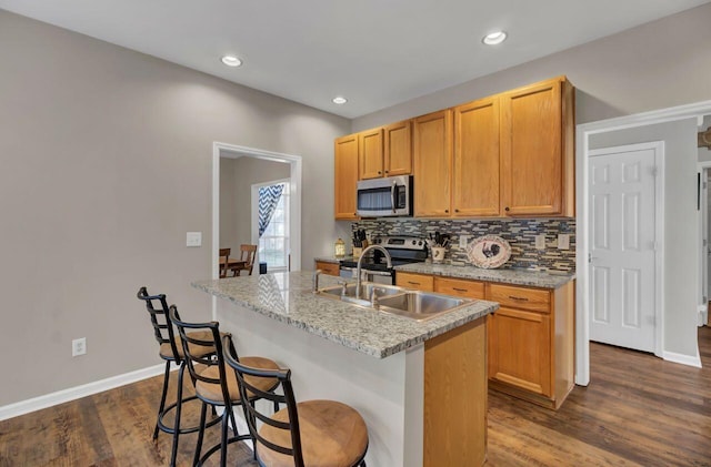 kitchen featuring sink, light stone counters, dark hardwood / wood-style floors, a center island with sink, and appliances with stainless steel finishes