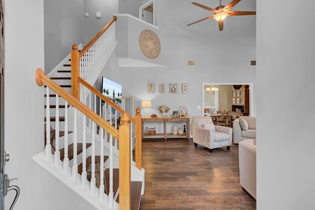 stairs featuring hardwood / wood-style floors, ceiling fan with notable chandelier, and a towering ceiling