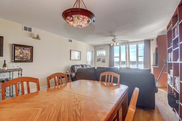 dining space featuring ceiling fan, a textured ceiling, light hardwood / wood-style floors, and a water view