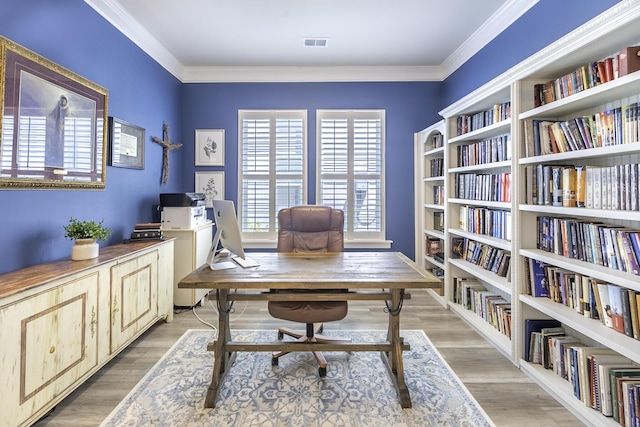 office space featuring light wood-style flooring, ornamental molding, and wall of books