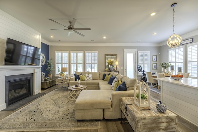 living area with ceiling fan, crown molding, a chandelier, dark wood finished floors, and a glass covered fireplace