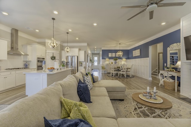 living room with crown molding, light wood-style flooring, a ceiling fan, wainscoting, and recessed lighting