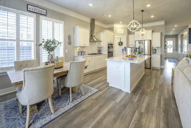 kitchen featuring wall chimney range hood, appliances with stainless steel finishes, ornamental molding, light countertops, and white cabinetry