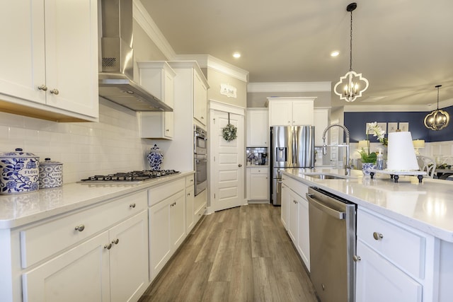 kitchen with wall chimney exhaust hood, appliances with stainless steel finishes, a sink, ornamental molding, and white cabinetry