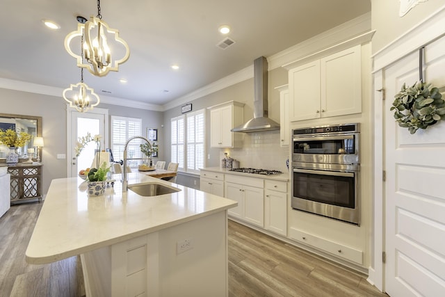 kitchen with a sink, wall chimney range hood, a chandelier, stainless steel appliances, and backsplash