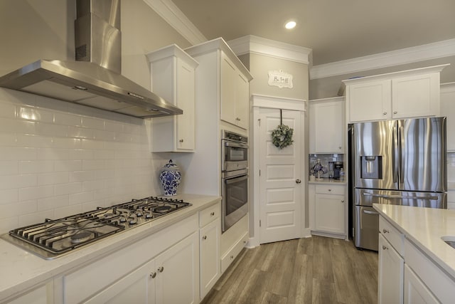 kitchen with stainless steel appliances, wall chimney range hood, backsplash, white cabinetry, and crown molding