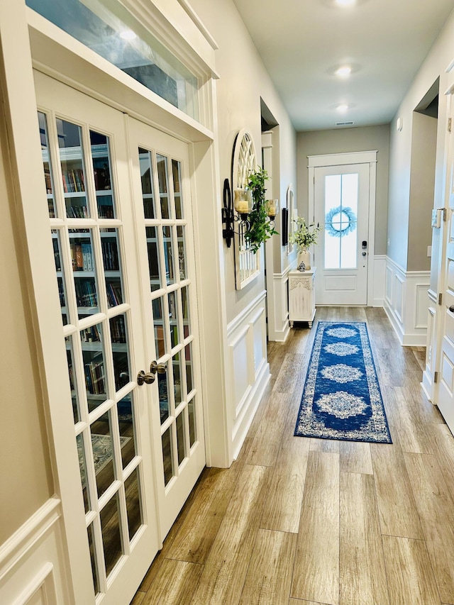 entrance foyer featuring a decorative wall, french doors, a wainscoted wall, and wood finished floors