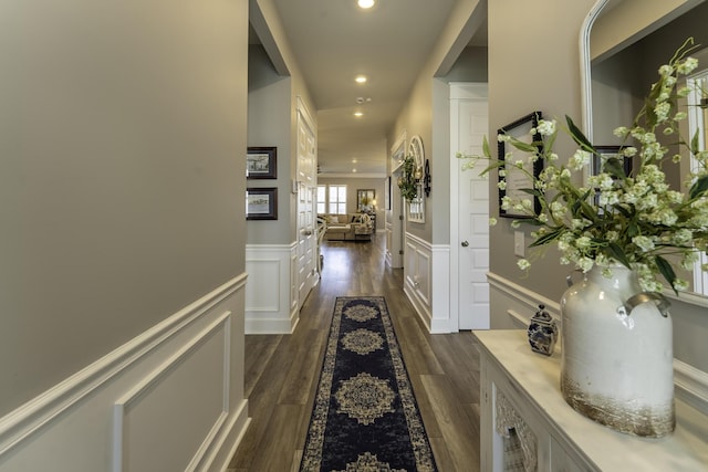 hallway with wainscoting, a decorative wall, recessed lighting, and dark wood-style flooring