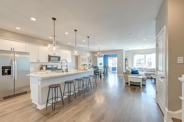 kitchen featuring pendant lighting, white cabinets, a spacious island, light hardwood / wood-style flooring, and stainless steel appliances