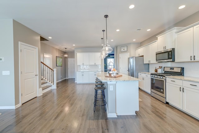 kitchen featuring a center island with sink, pendant lighting, white cabinets, and stainless steel appliances