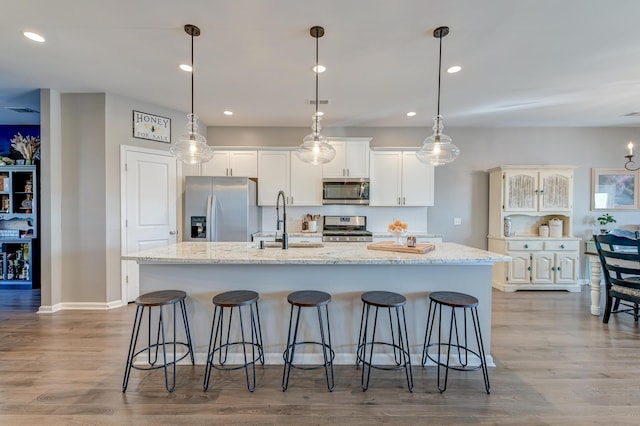 kitchen featuring a kitchen island with sink, pendant lighting, white cabinets, and stainless steel appliances