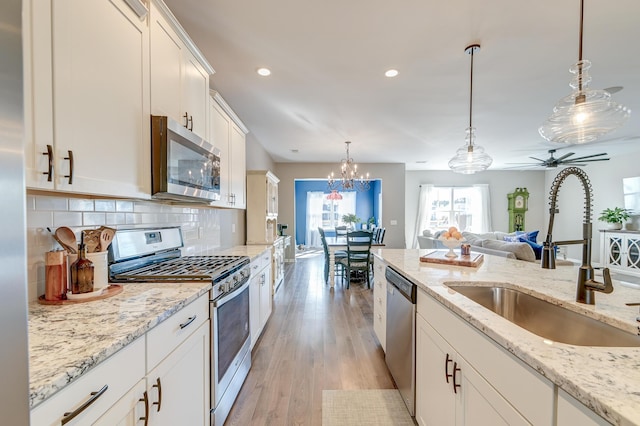 kitchen featuring white cabinets, sink, light hardwood / wood-style flooring, decorative light fixtures, and stainless steel appliances