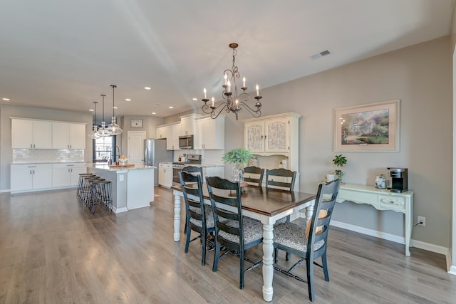 dining space with sink, light hardwood / wood-style flooring, and an inviting chandelier