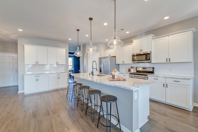 kitchen featuring stainless steel appliances, white cabinetry, hanging light fixtures, and light hardwood / wood-style floors