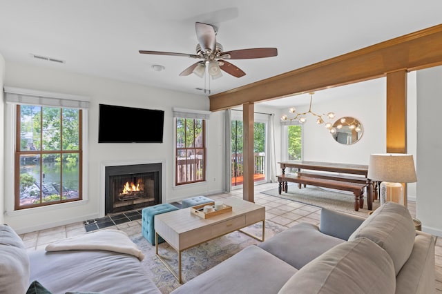 tiled living room with plenty of natural light, visible vents, ceiling fan with notable chandelier, and a lit fireplace