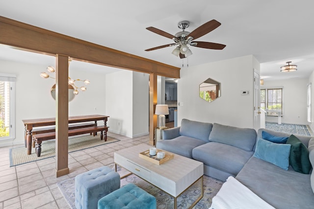 living room featuring ceiling fan with notable chandelier, light tile patterned floors, and baseboards