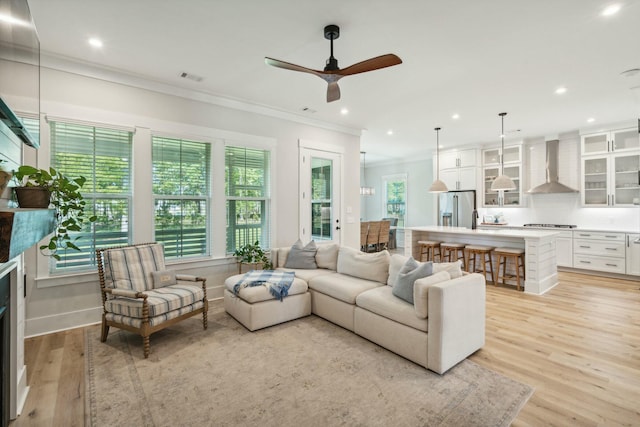 living area with light wood finished floors, plenty of natural light, a fireplace, and ornamental molding