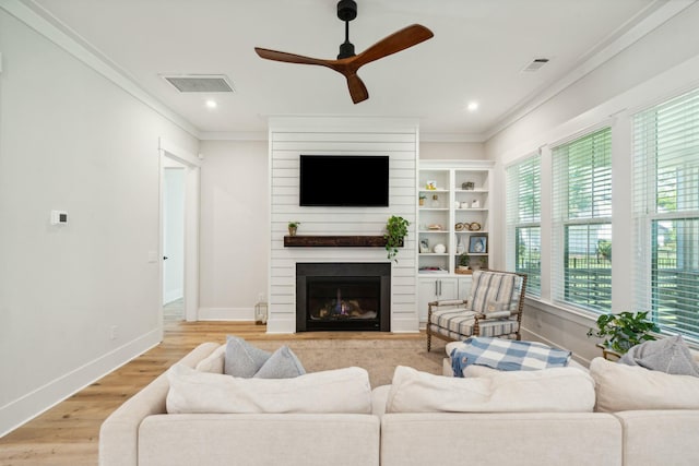 living area with a large fireplace, visible vents, crown molding, and light wood finished floors