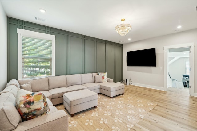 living room with plenty of natural light, light wood-type flooring, visible vents, and a decorative wall