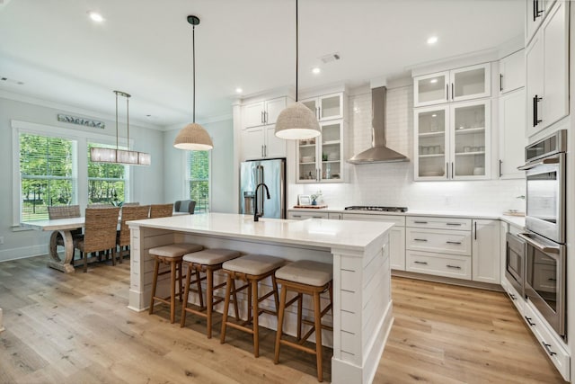 kitchen with stainless steel appliances, tasteful backsplash, ornamental molding, a kitchen island with sink, and wall chimney exhaust hood