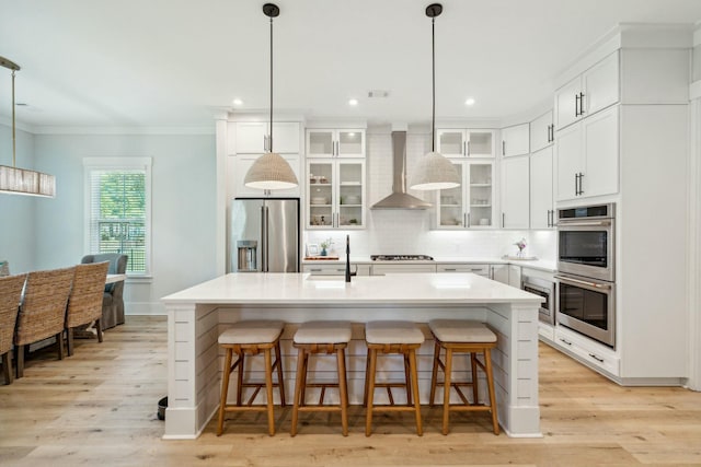 kitchen with tasteful backsplash, appliances with stainless steel finishes, ornamental molding, a kitchen island with sink, and wall chimney exhaust hood