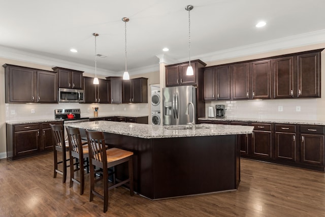 207 Brutus Ln, Summerville, SC 29485 - kitchen featuring stainless steel appliances, stacked washer / dryer, a kitchen island with sink, dark brown cabinets, and decorative backsplash